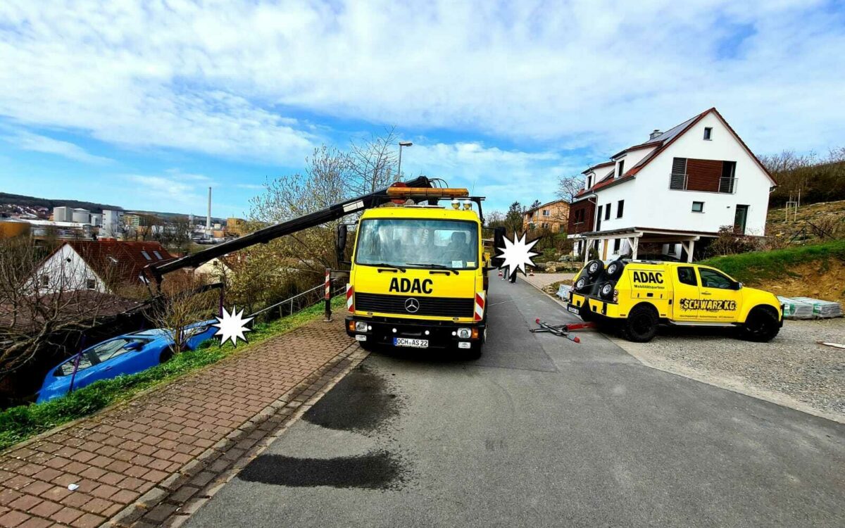 Zwei gelbe ADAC-Fahrzeuge stehen auf einer Straße, links ein Auto am Abhang Zwei gelbe ADAC-Fahrzeuge stehen auf einer Straße, links ein Auto am Abhang
